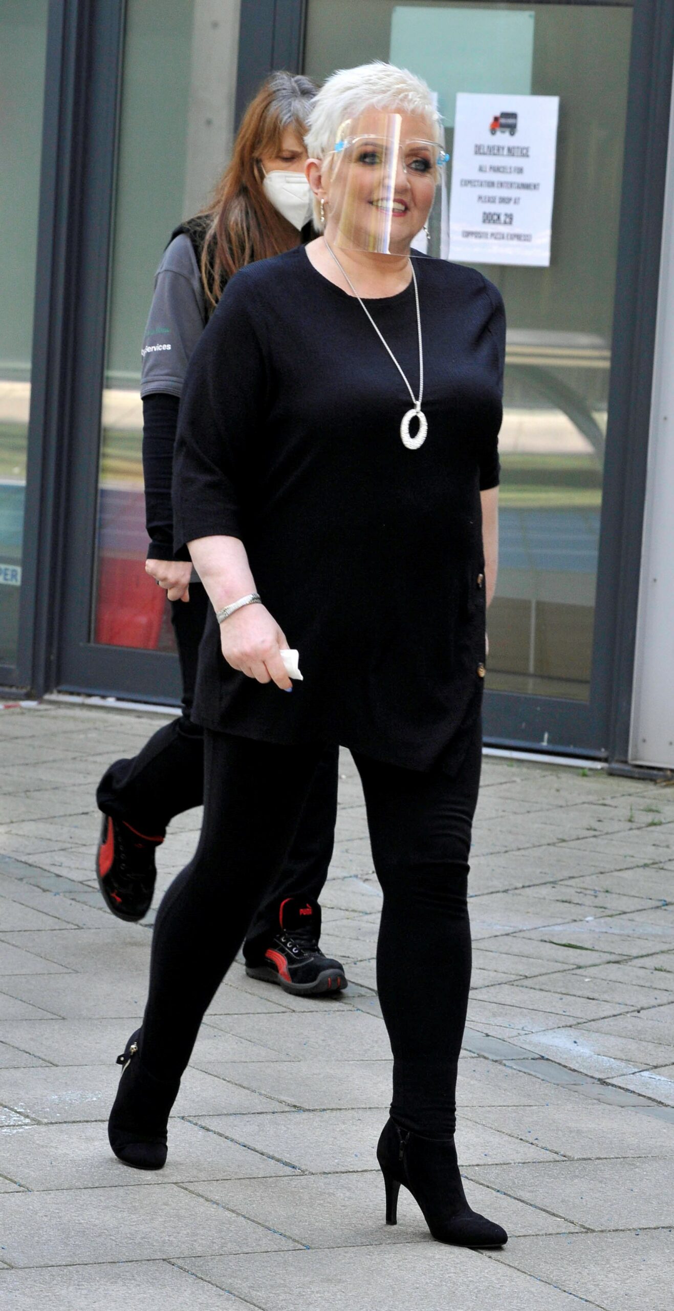 Linda Nolan smiling in black outfit with face mask