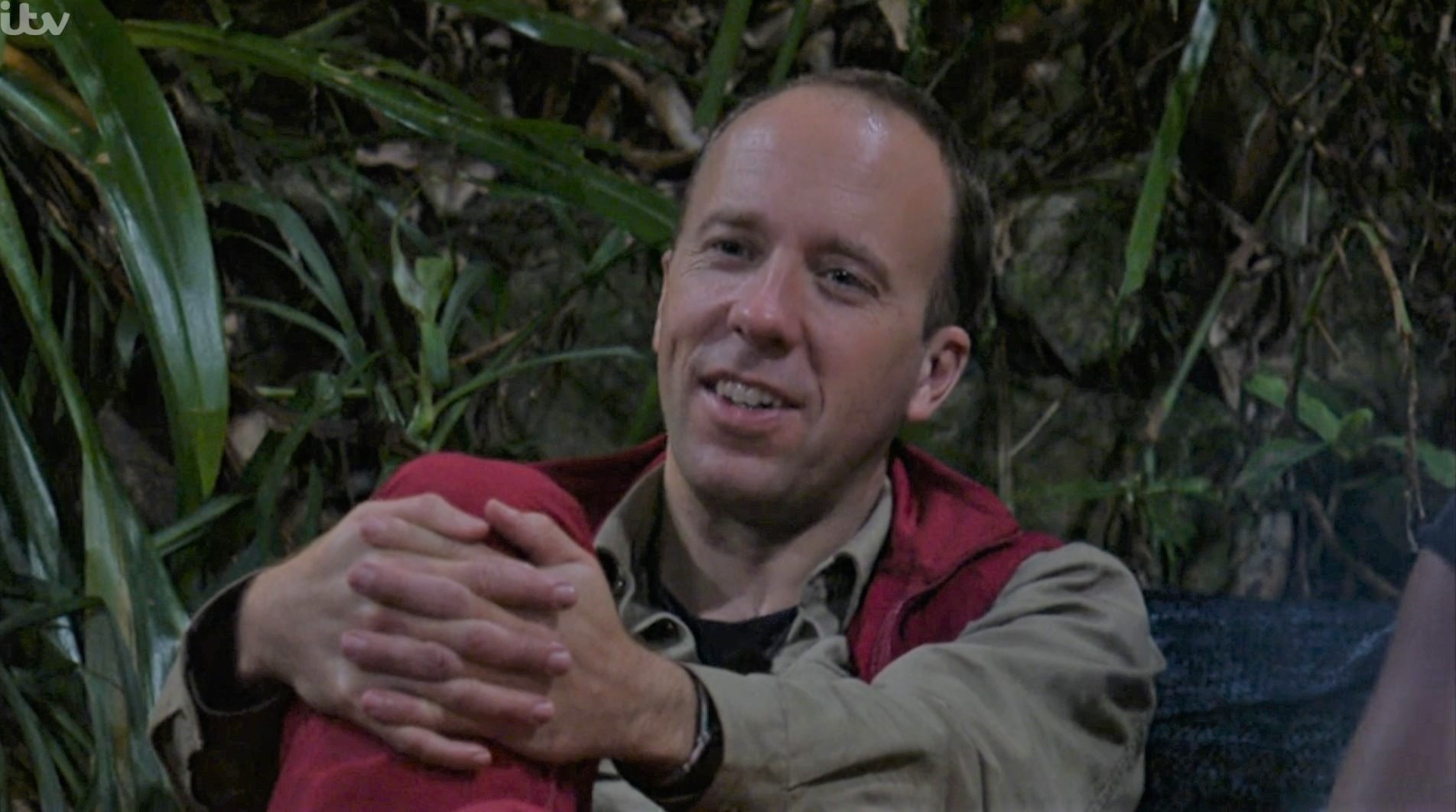 Matt Hancock wraps his hands around his knees as he leans back and smiles