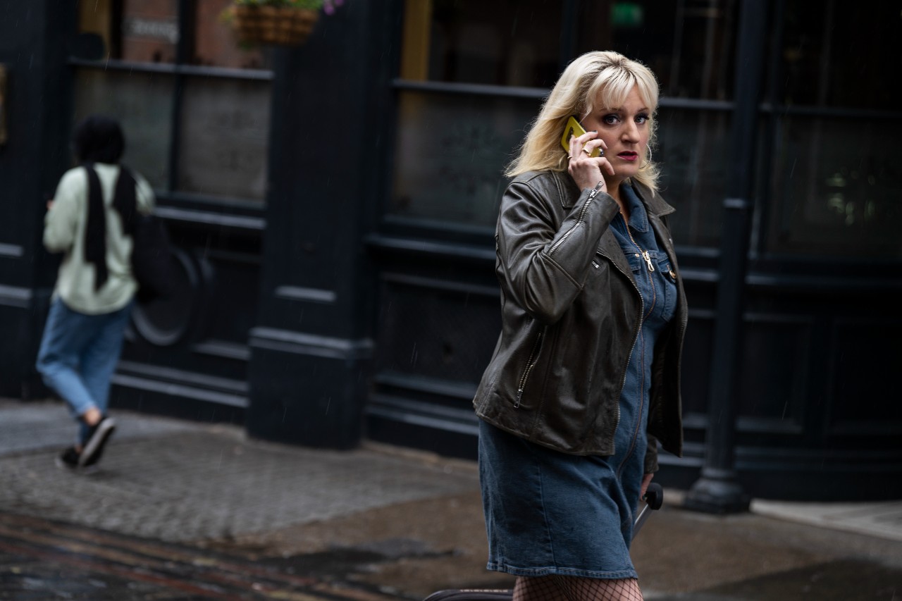 Daisy May Cooper holds her phone up in Rain Dogs