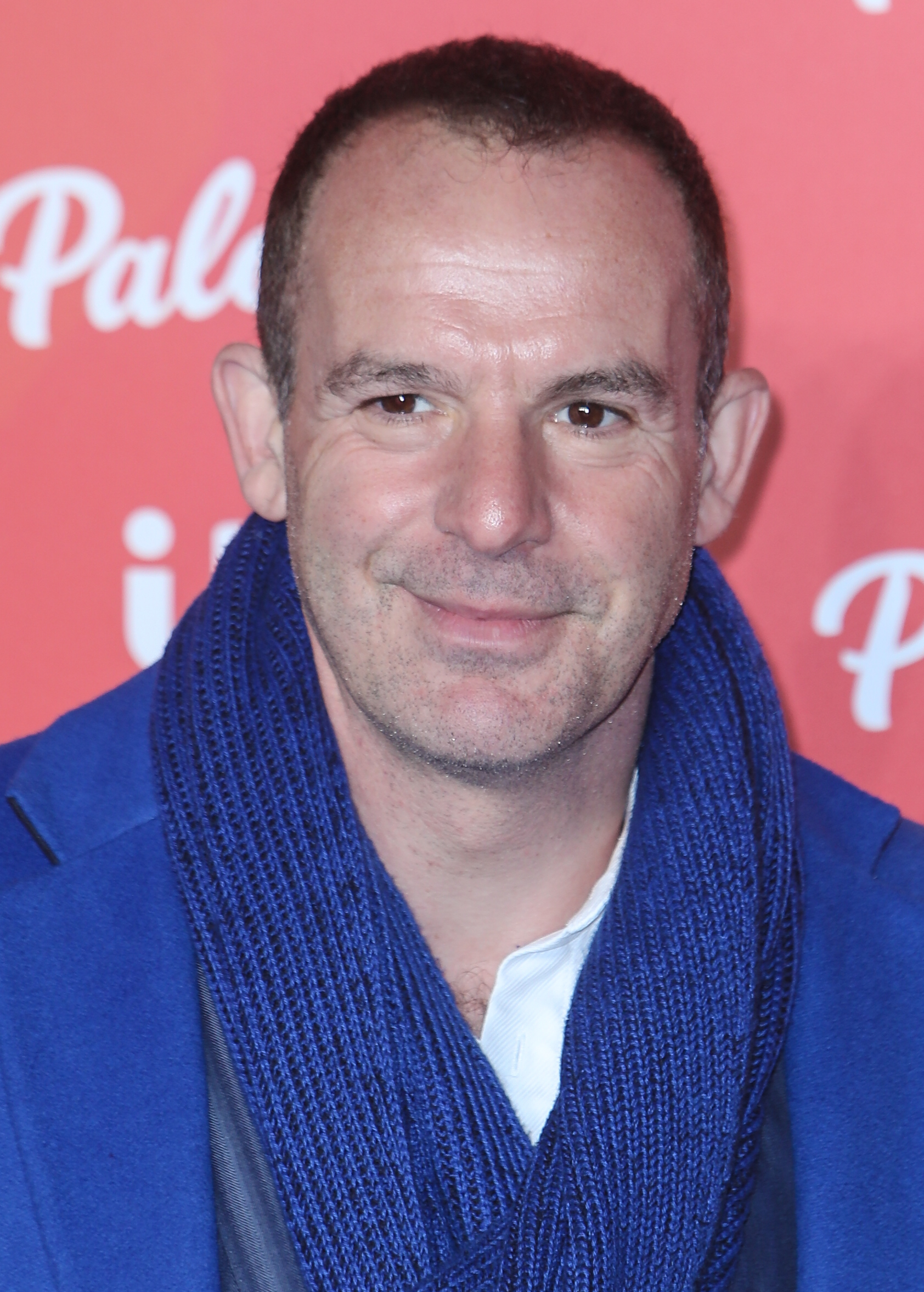 Martin Lewis at red carpet event wearing blue scarf and coat. 