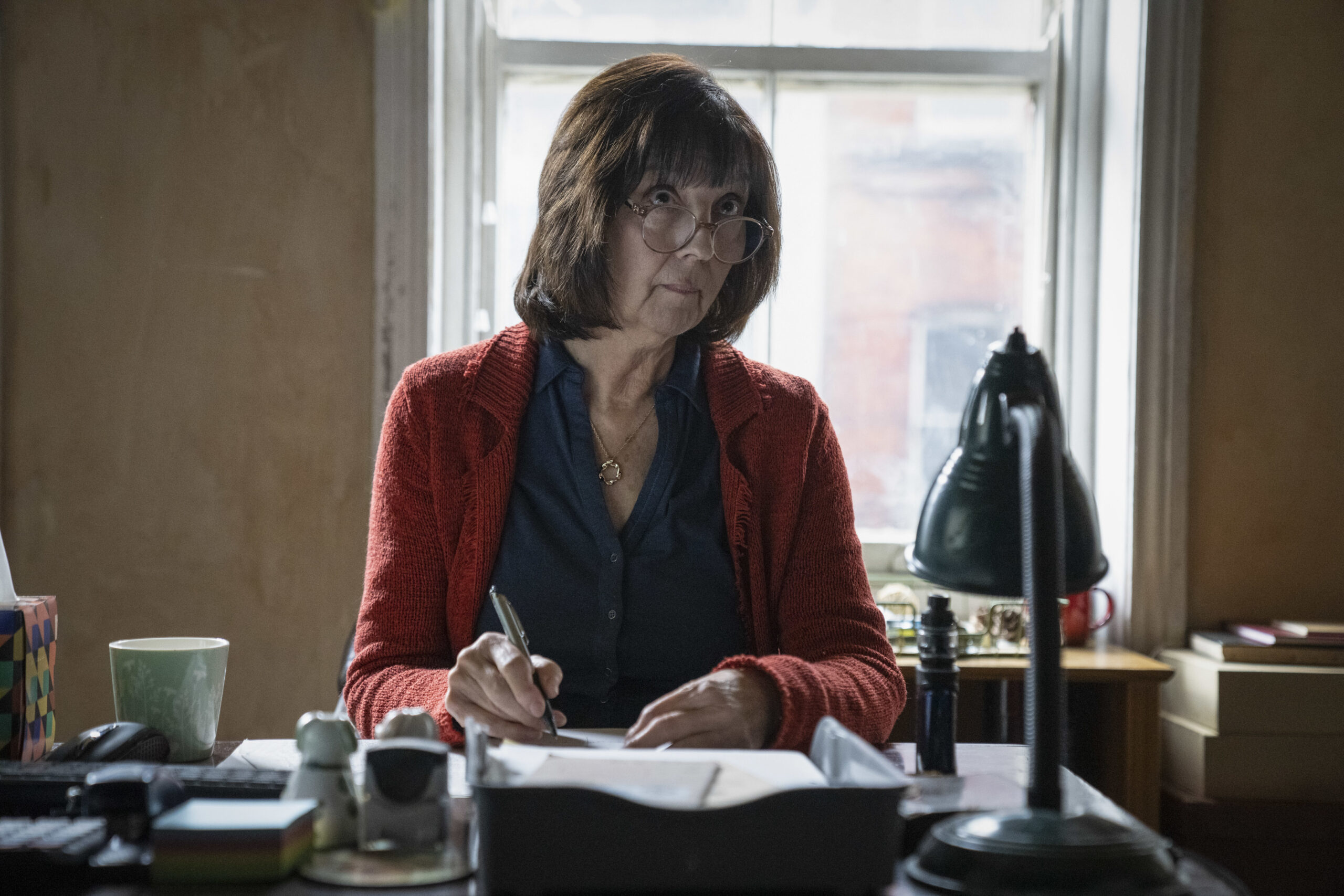 Pat Chauncey sits at her desk in Strike Troubled Blood cast