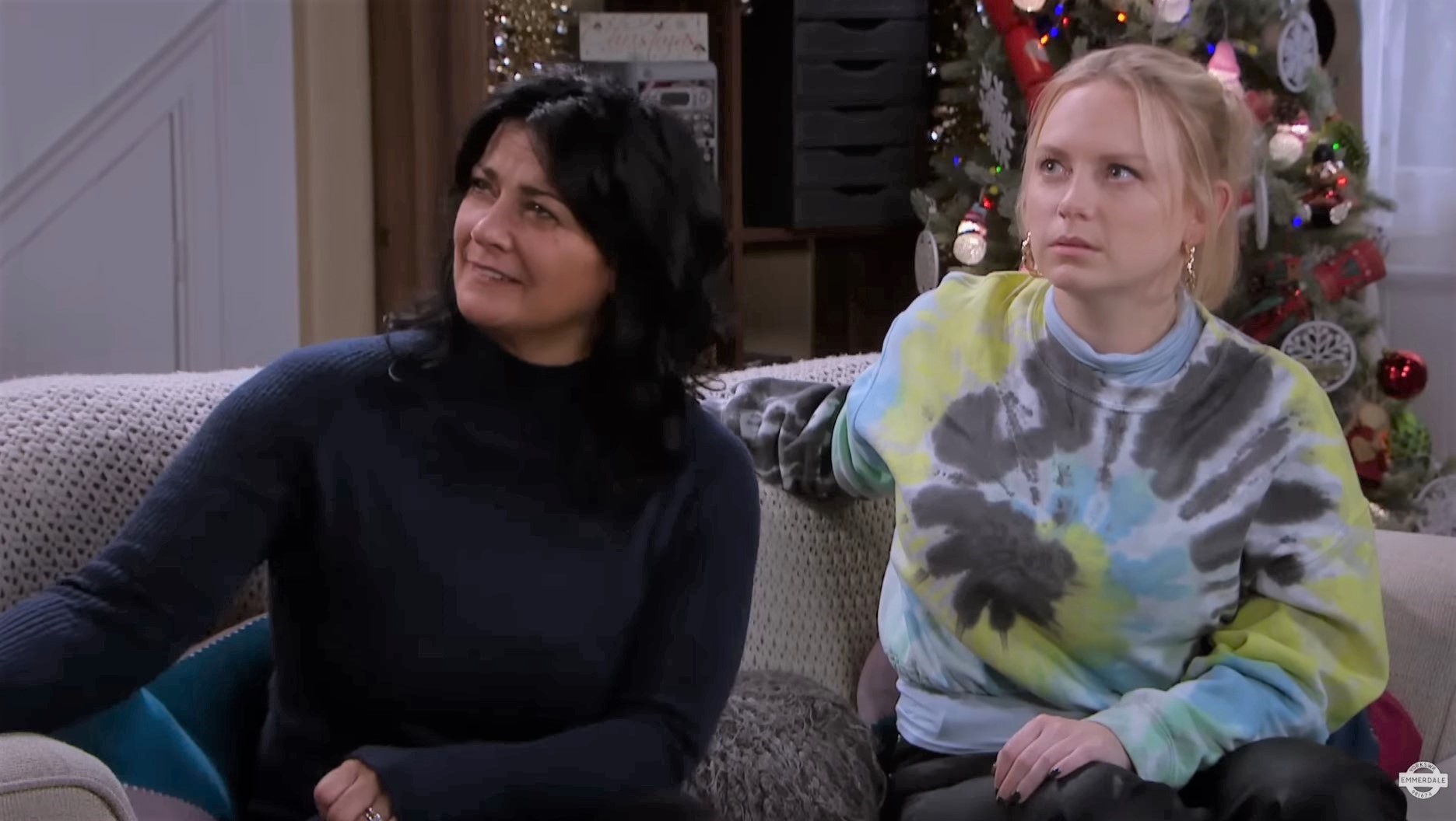 Emmerdale's Moira and Amy sit on the sofa and try to look shocked and confused