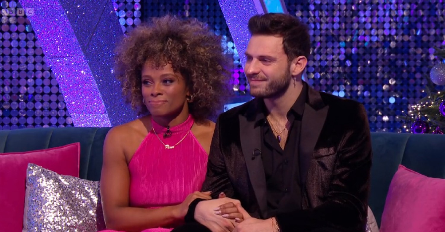 Fleur East and Vito hold arms and sit on sofa on Strictly It Takes Two