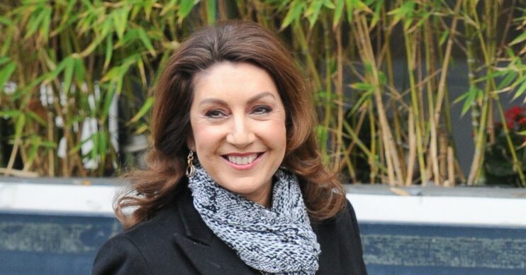Jane McDonald smiling at camera wearing black jacket and grey scarf