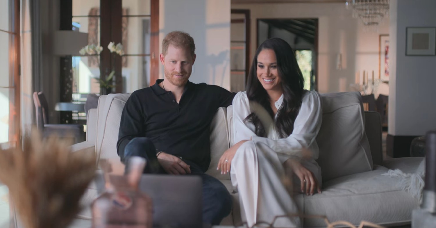 Prince Harry and Meghan Markle on a couch smiling in their new documentary 