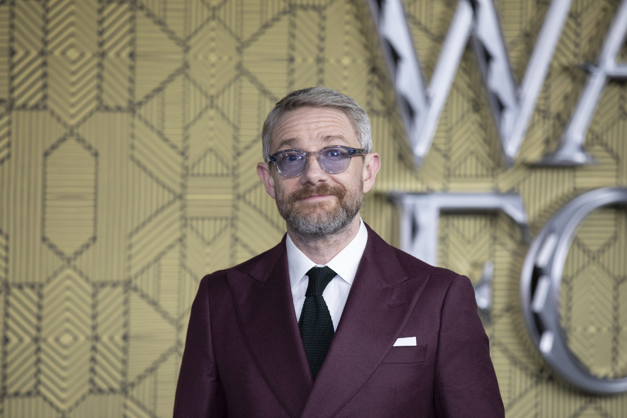 Martin Freeman smiling on the red carpet wearing purple sunglasses