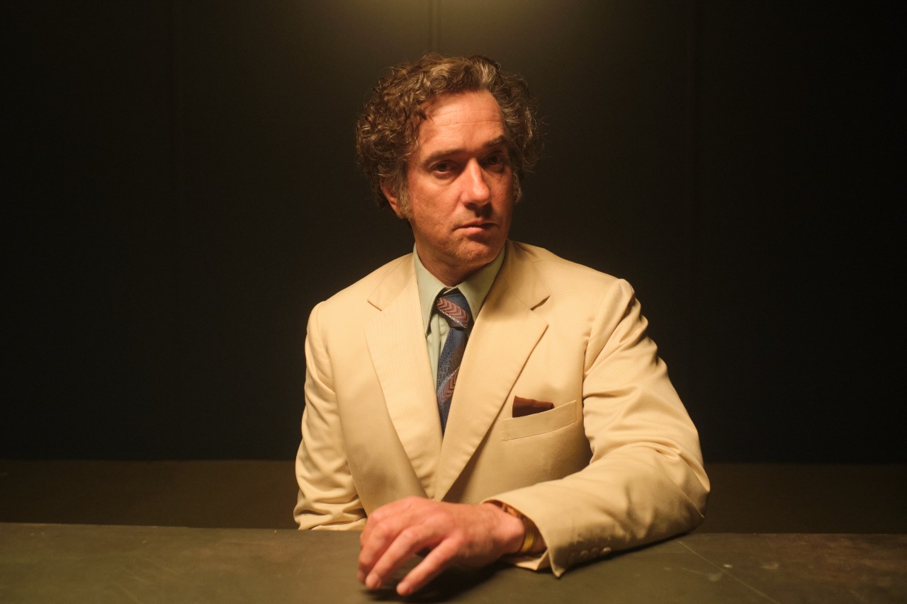John Stonehouse leans over a table in a white suit