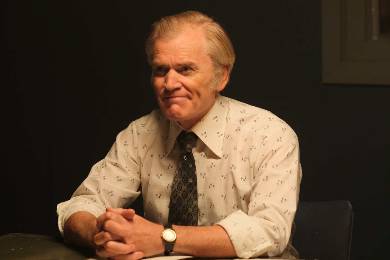 Mackenzie smiles sitting a table in a police interview