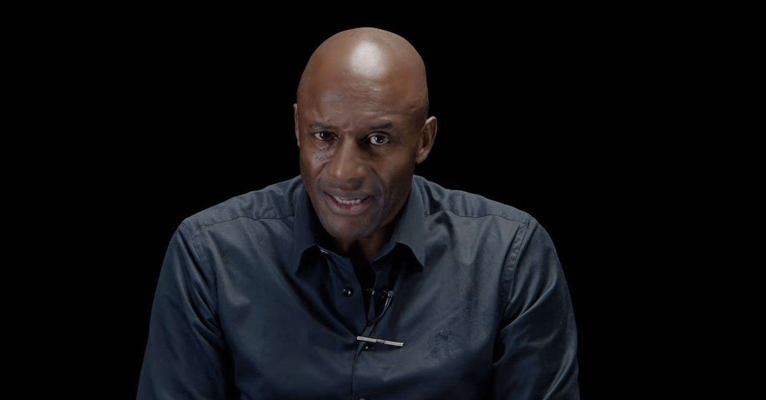 John looks to camera on a black background