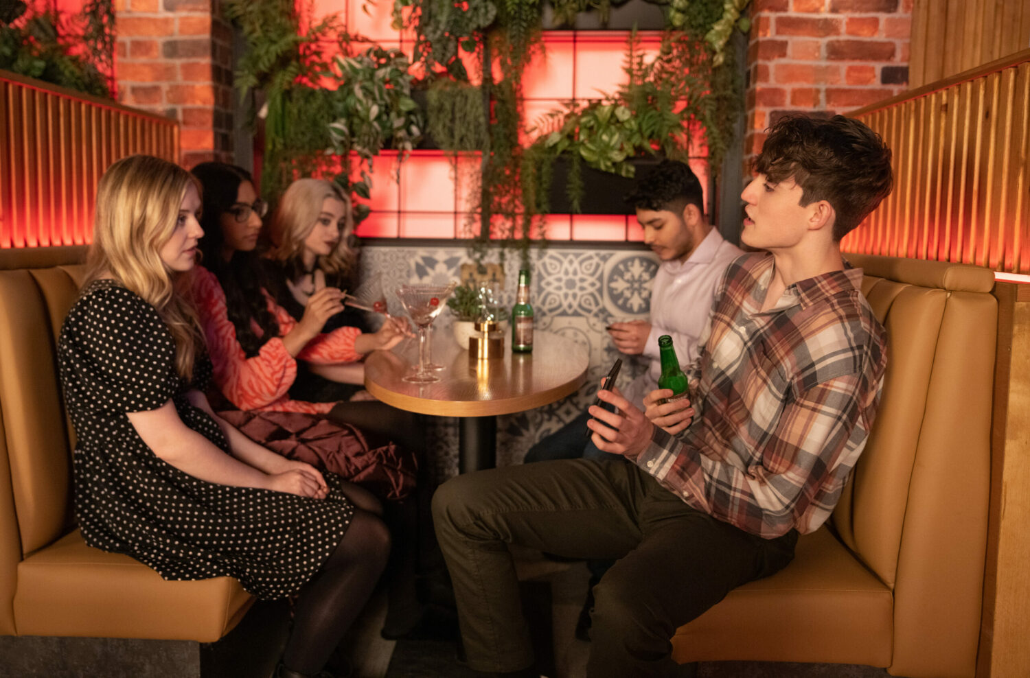 Aaron and Summer argue in a booth in the bistro, surrounded by their friends on Corrie