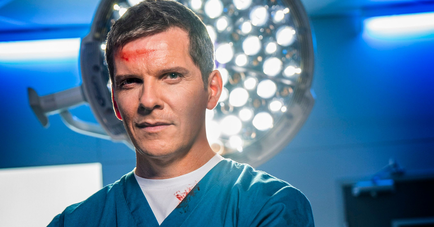 Casualty's Max is wearing scrubs with blood on his head