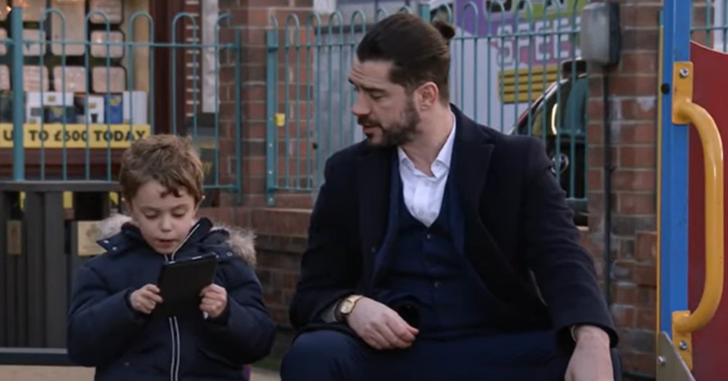 Coronation Street's Adam has a man bun whilst talking to Harry at the playground
