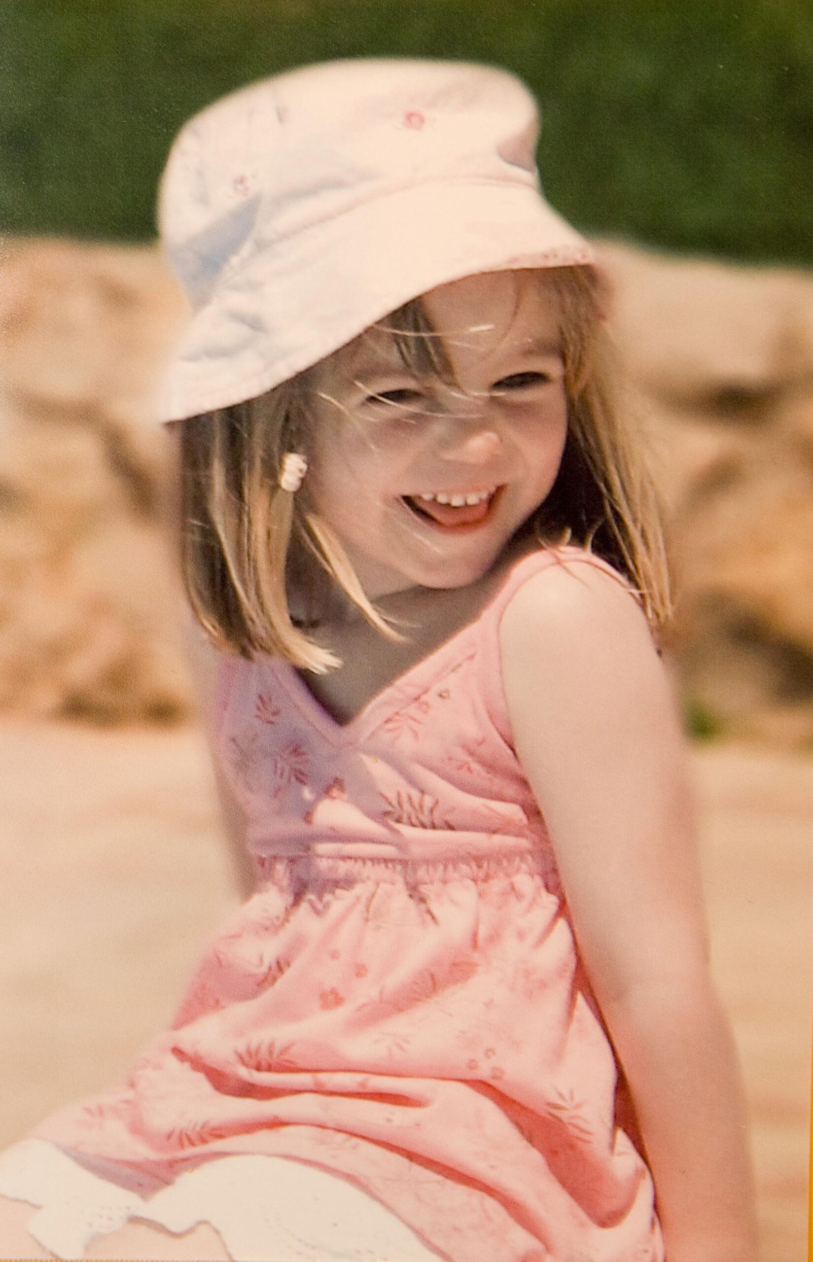 Madeleine McCann smiling in a pink hat and dress