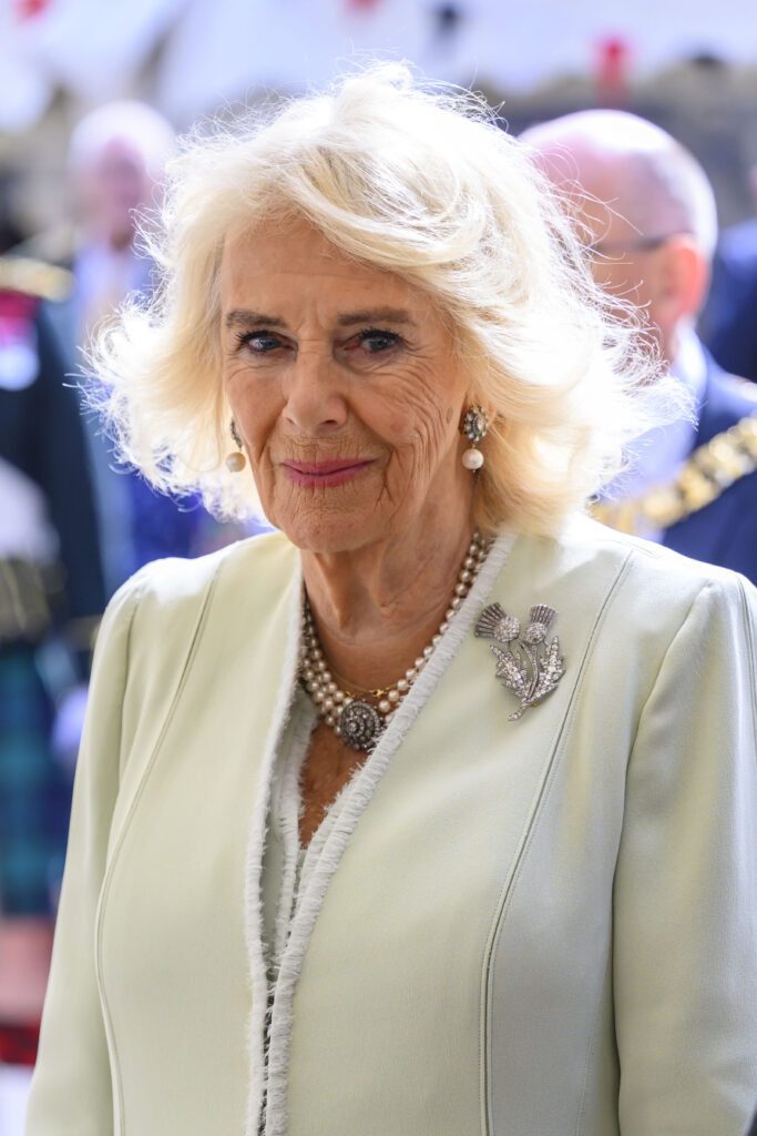 Queen Camilla wears a white coat and smiles