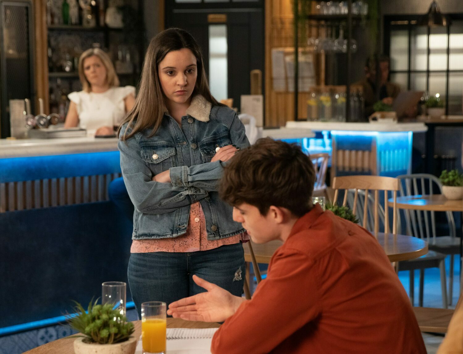 Coronation Street's Amy has her arms folded whilst looking at Aaron in the Bistro