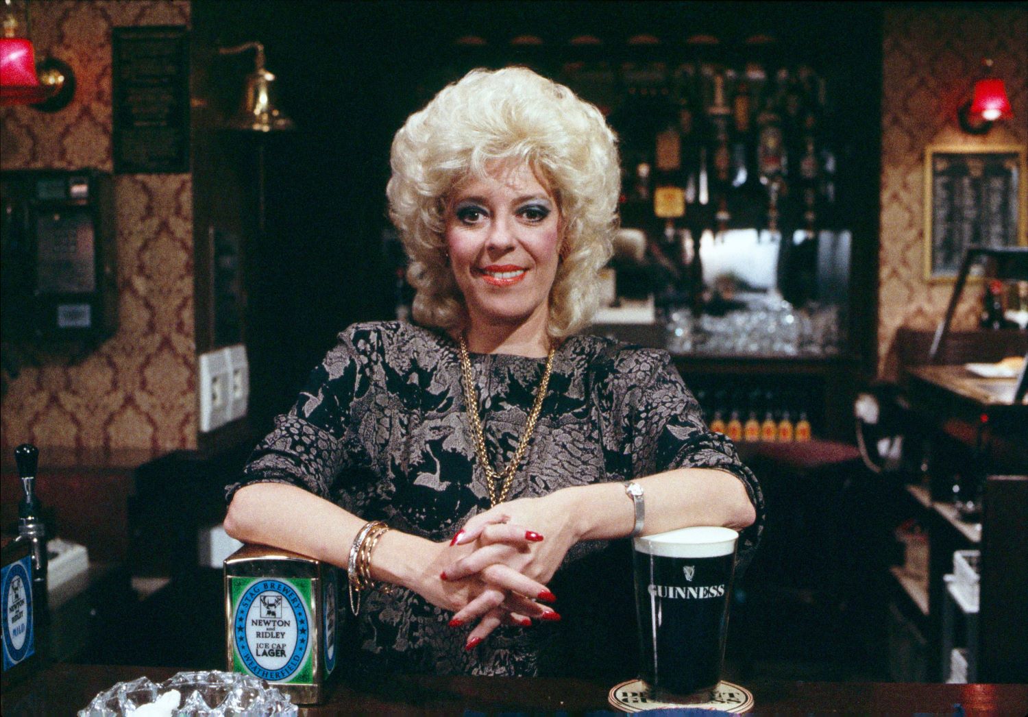 Bet Lynch behind the bar of the Rovers smiling in Coronation Street