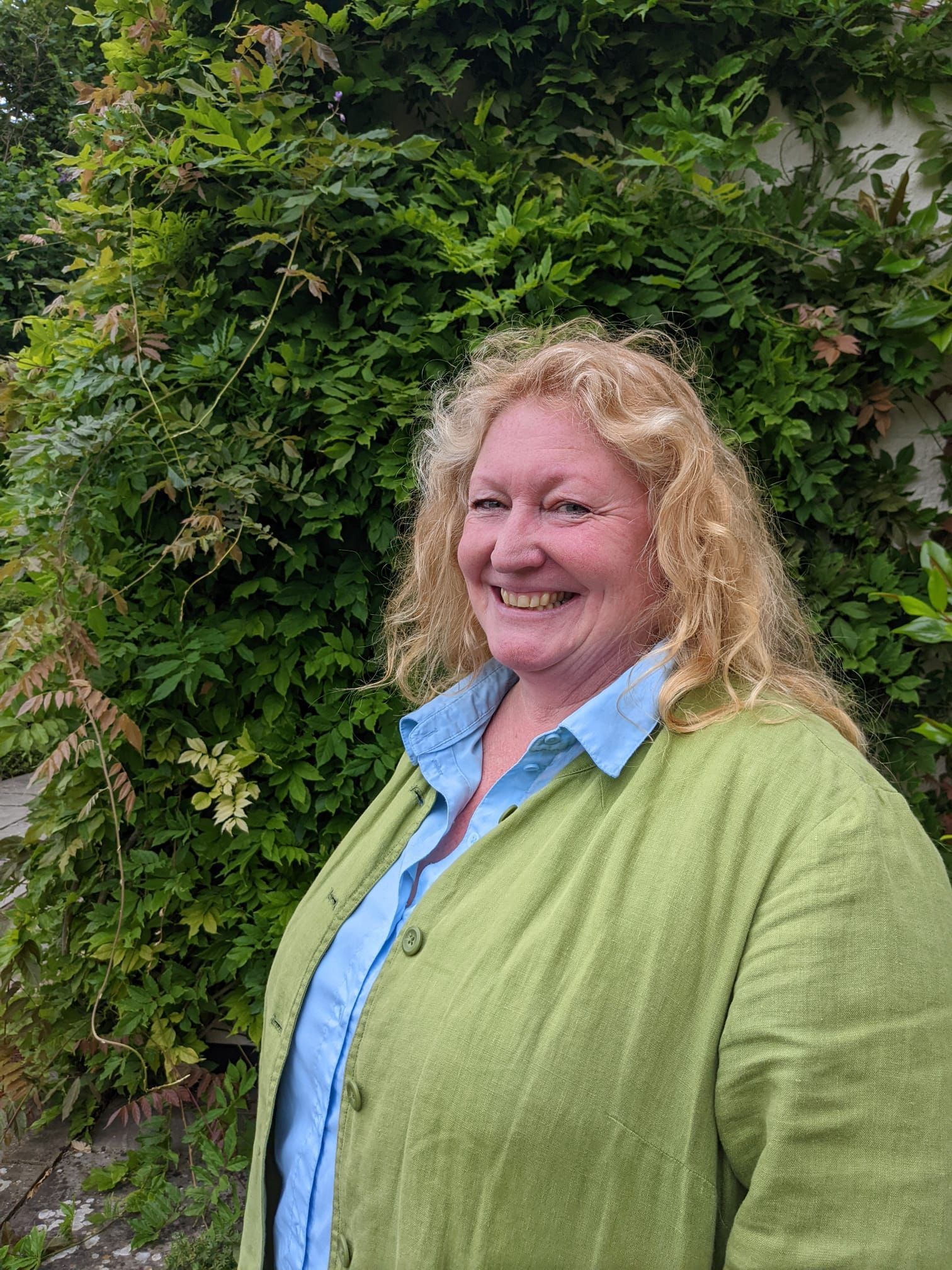 Charlie Dimmock smiling standing by a green hedge