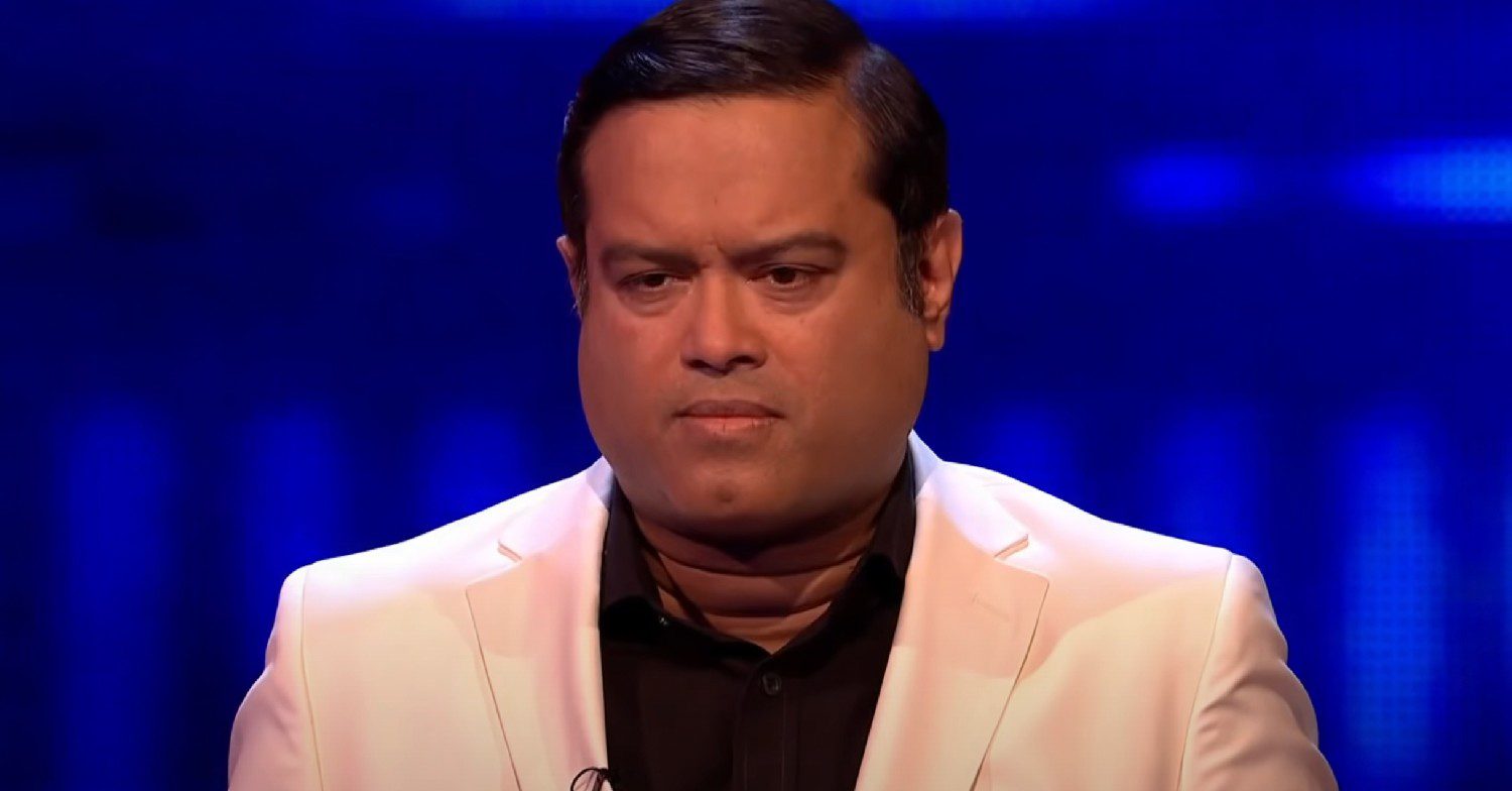Paul Sinha sat in a white suit while on the ITV show The Chase