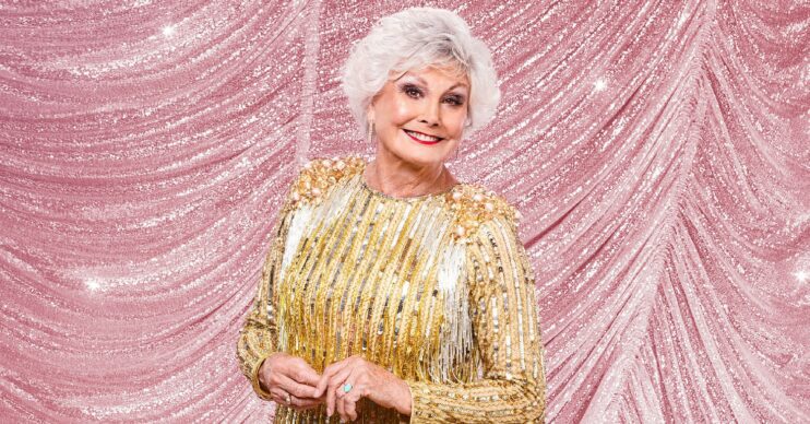 Strictly star Angela Rippon smiles in her promo shot in a gold dress on a pink sparkly background