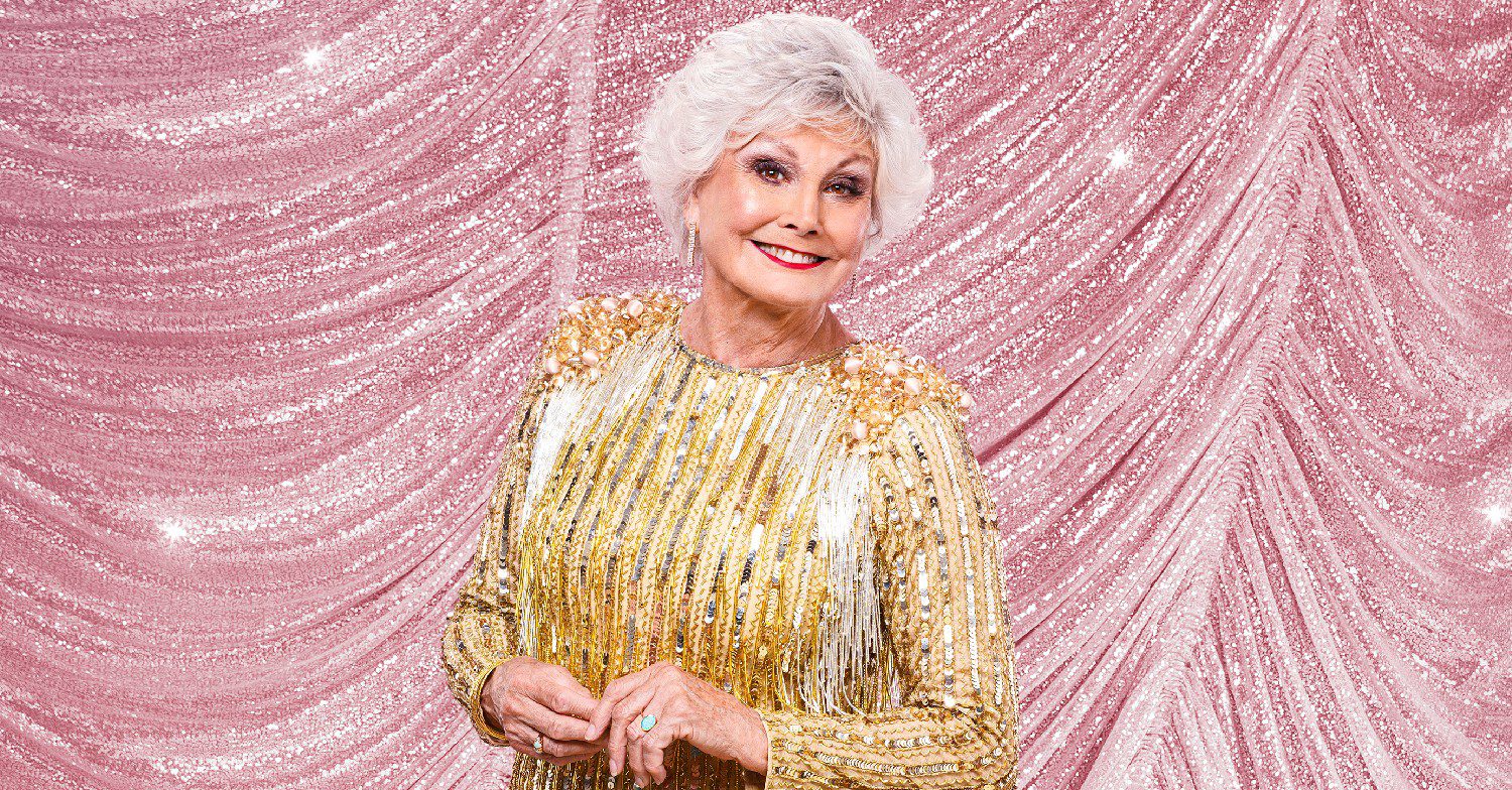 Strictly star Angela Rippon smiles in her promo shot in a gold dress on a pink sparkly background