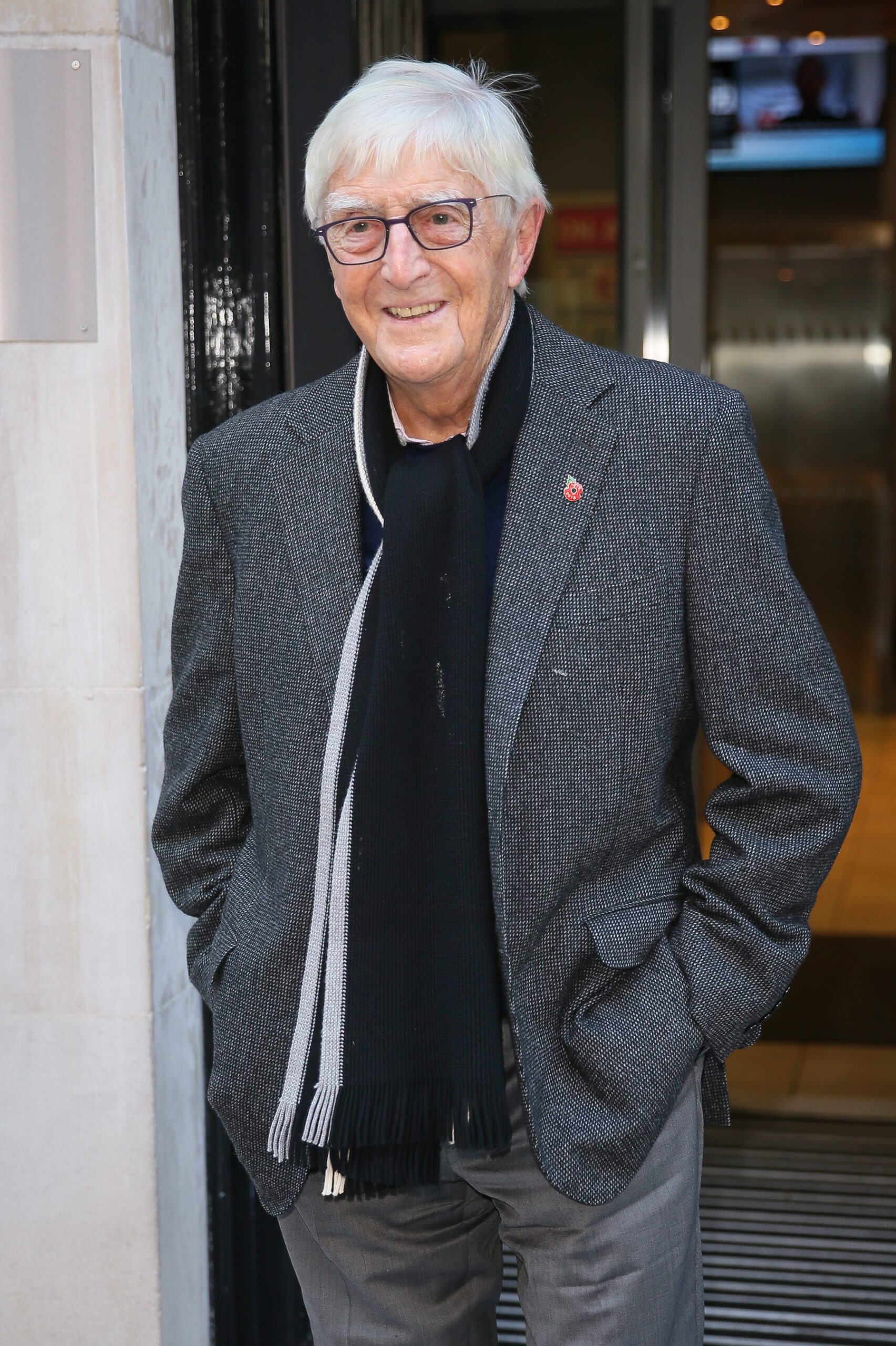 Sir Michael Parkinson smiling wearing a grey coat