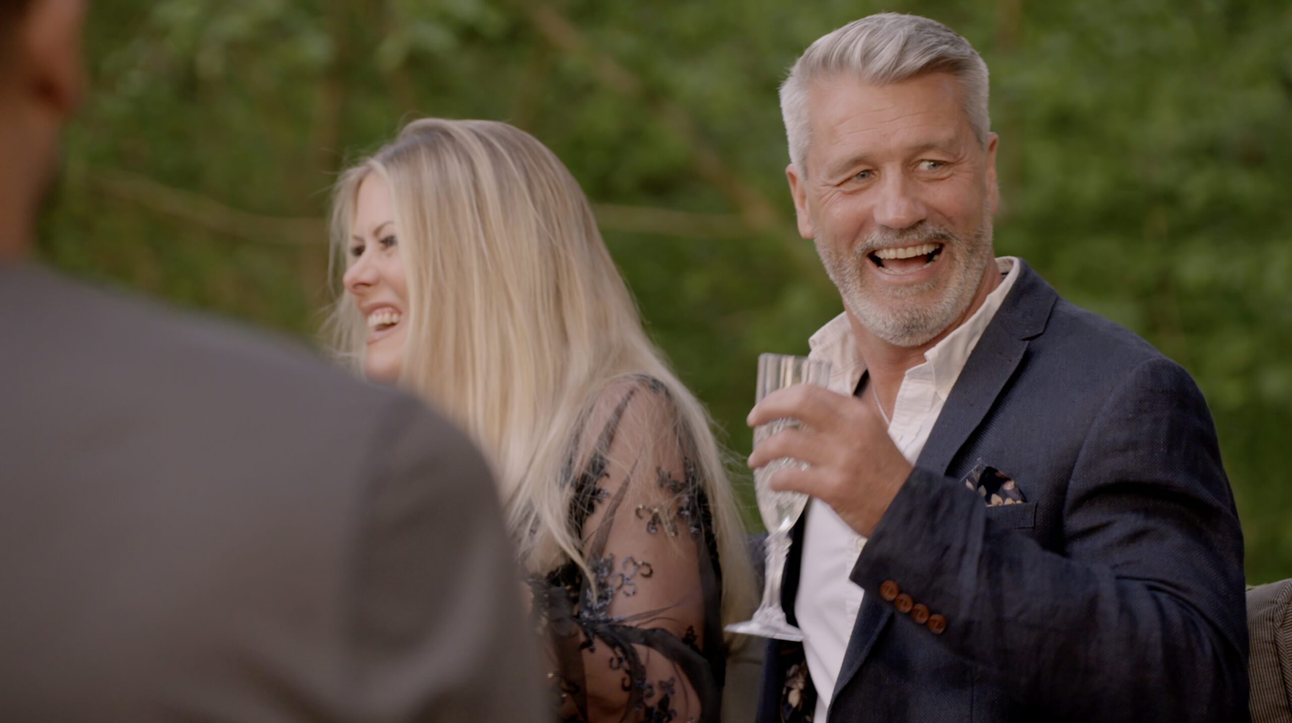 Roger smiling holding a champagne glass on My Mum Your Dad