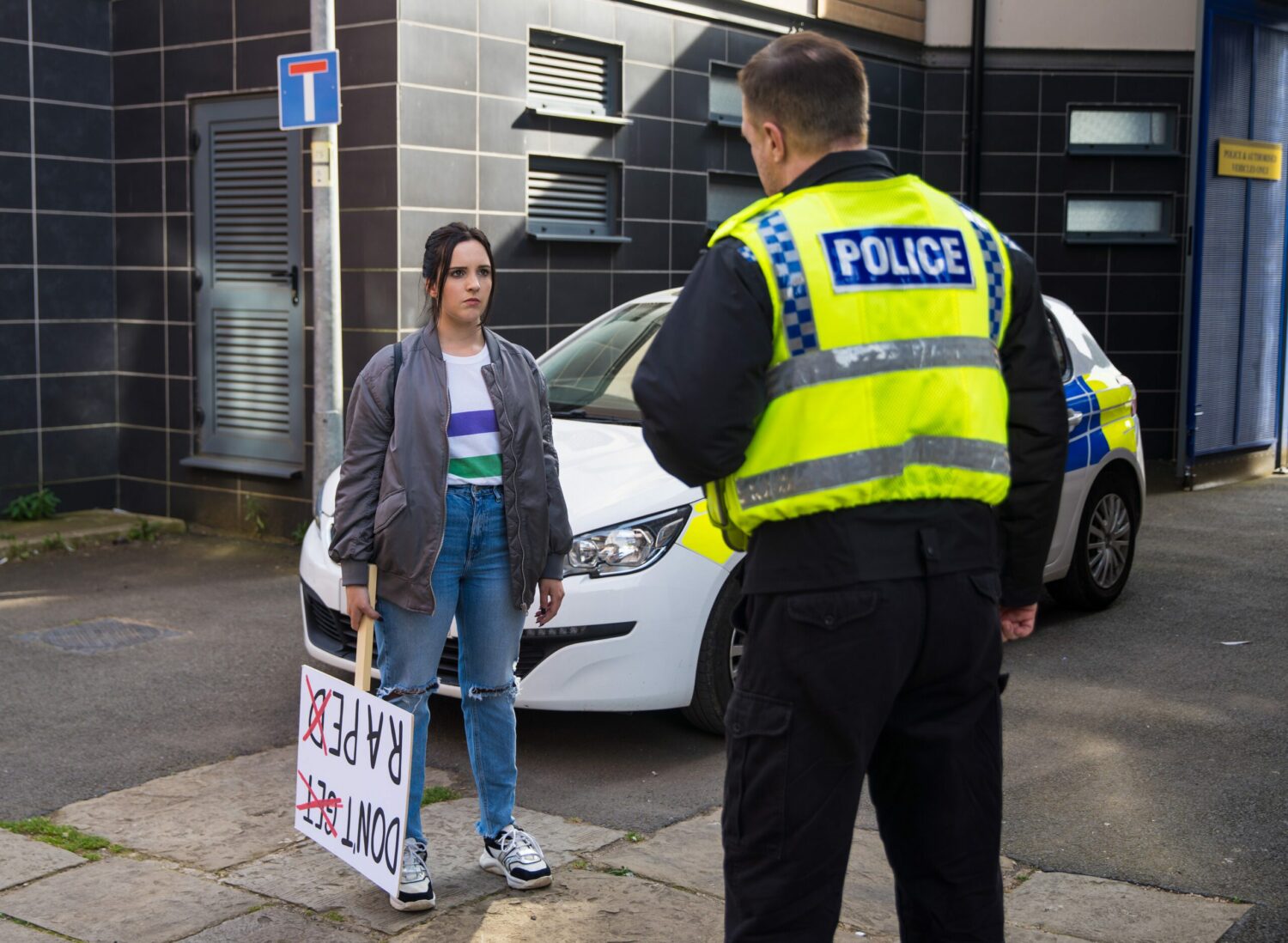 Coronation Street's Amy is holding a placard whilst standing in front of a police officer
