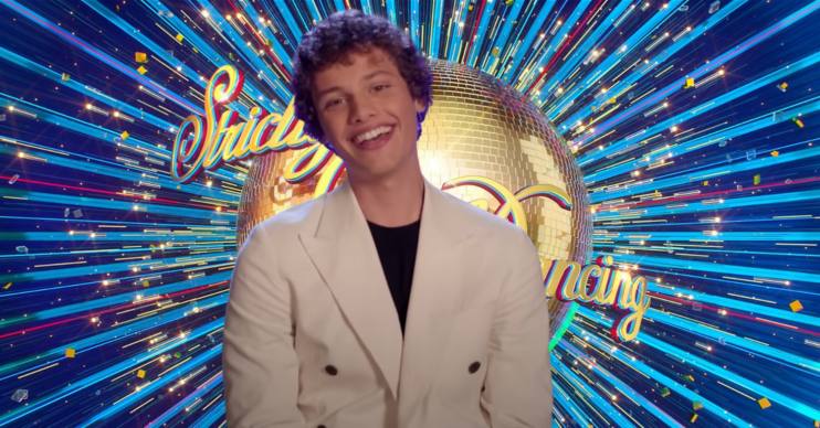 Bobby Brazier smiling in a cream suit while standing in front of the Strictly Come Dancing logo