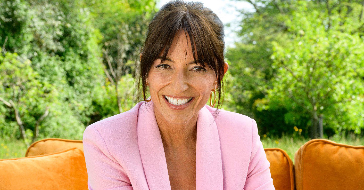 TV presenter Davina McCall sat smiling while wearing a pink suit advertising the ITV show My Mum Your Dad