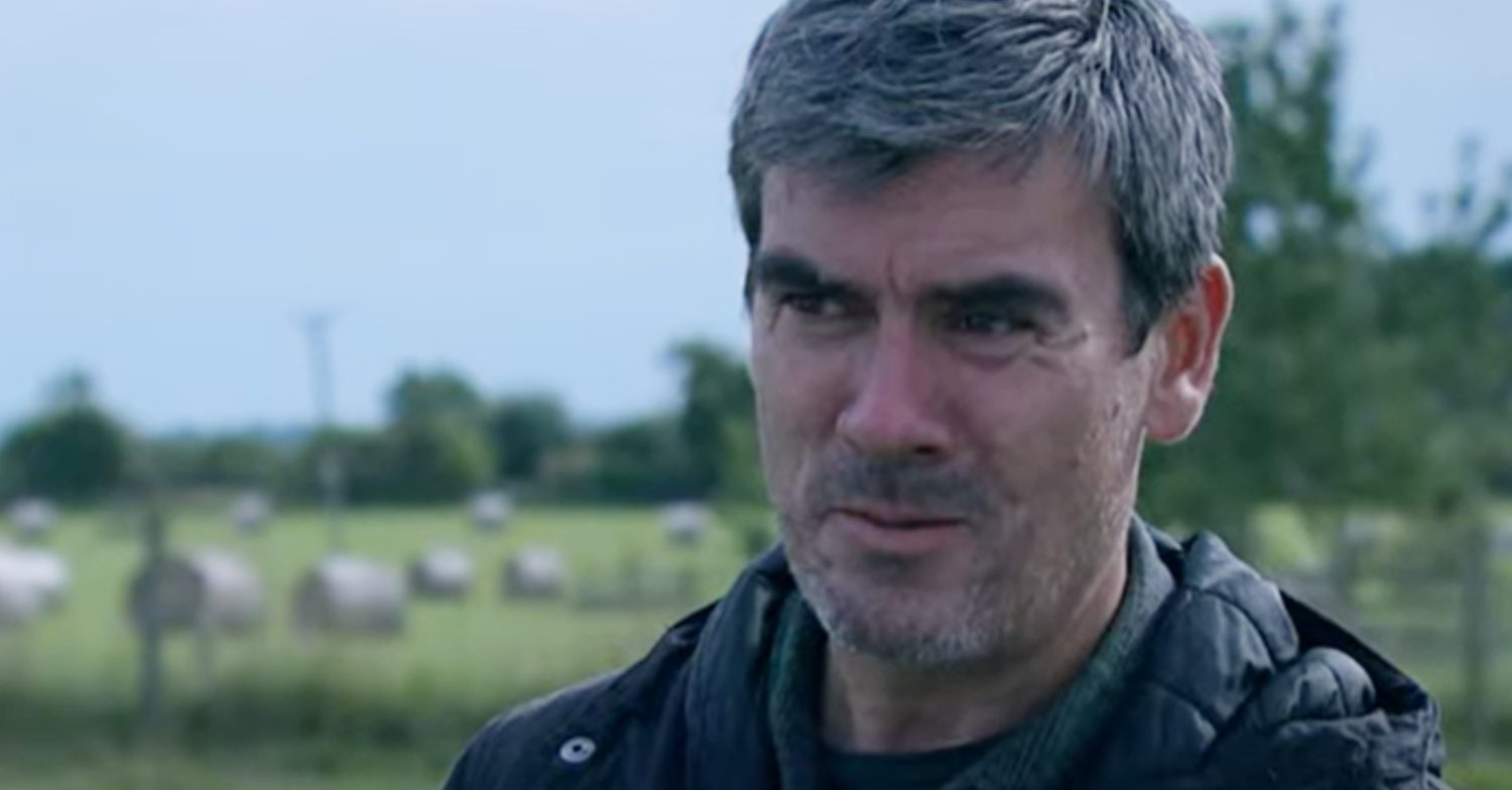 Emmerdale's Cain is serious whilst standing in a field