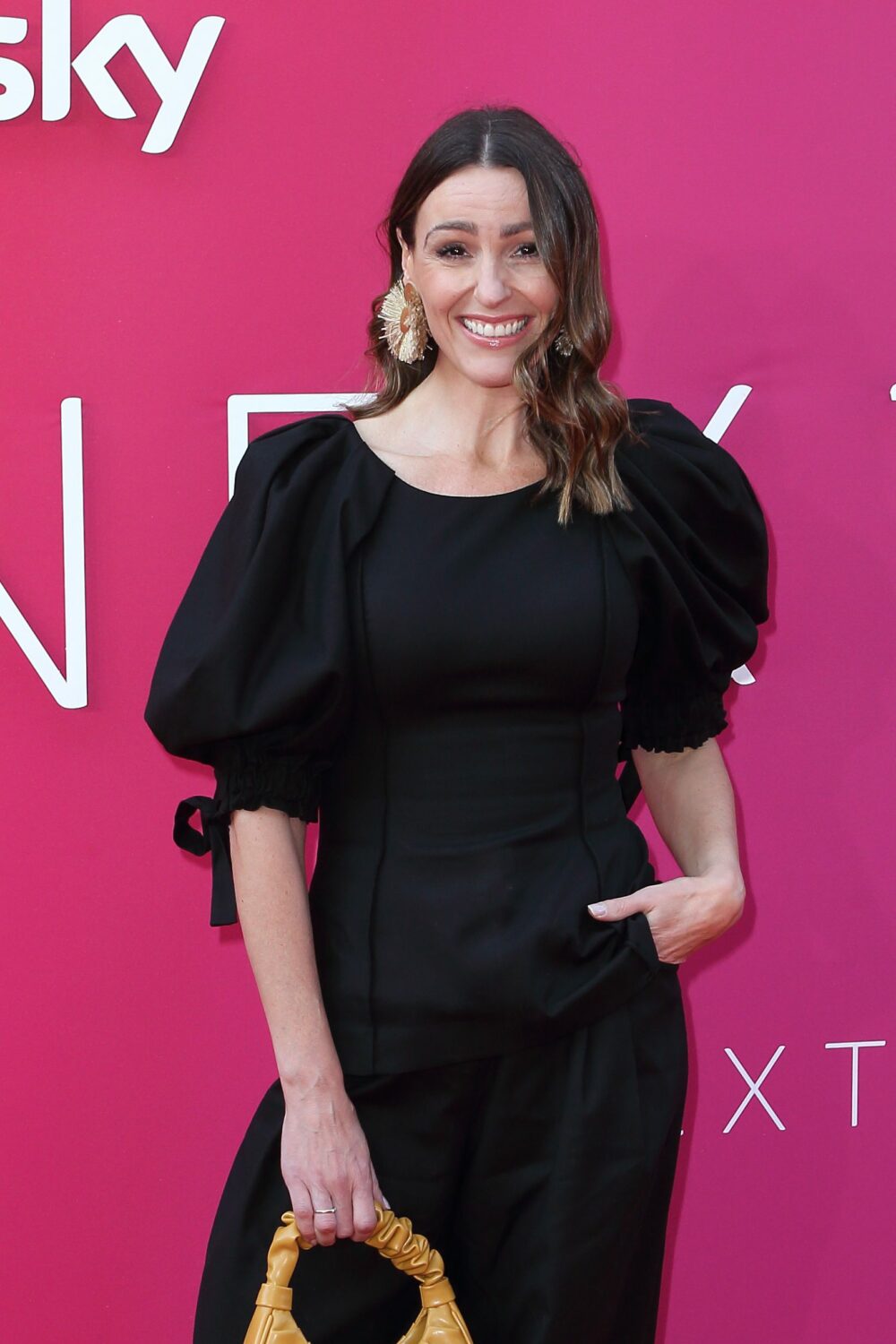 Suranne Jones in black jumpsuit beams on the red carpet in front of a pink Sky branding board