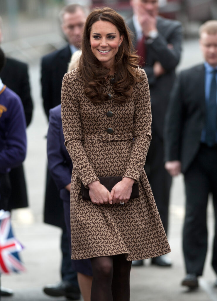 Kate Middleton wears a brown dress and smiles at the camera
