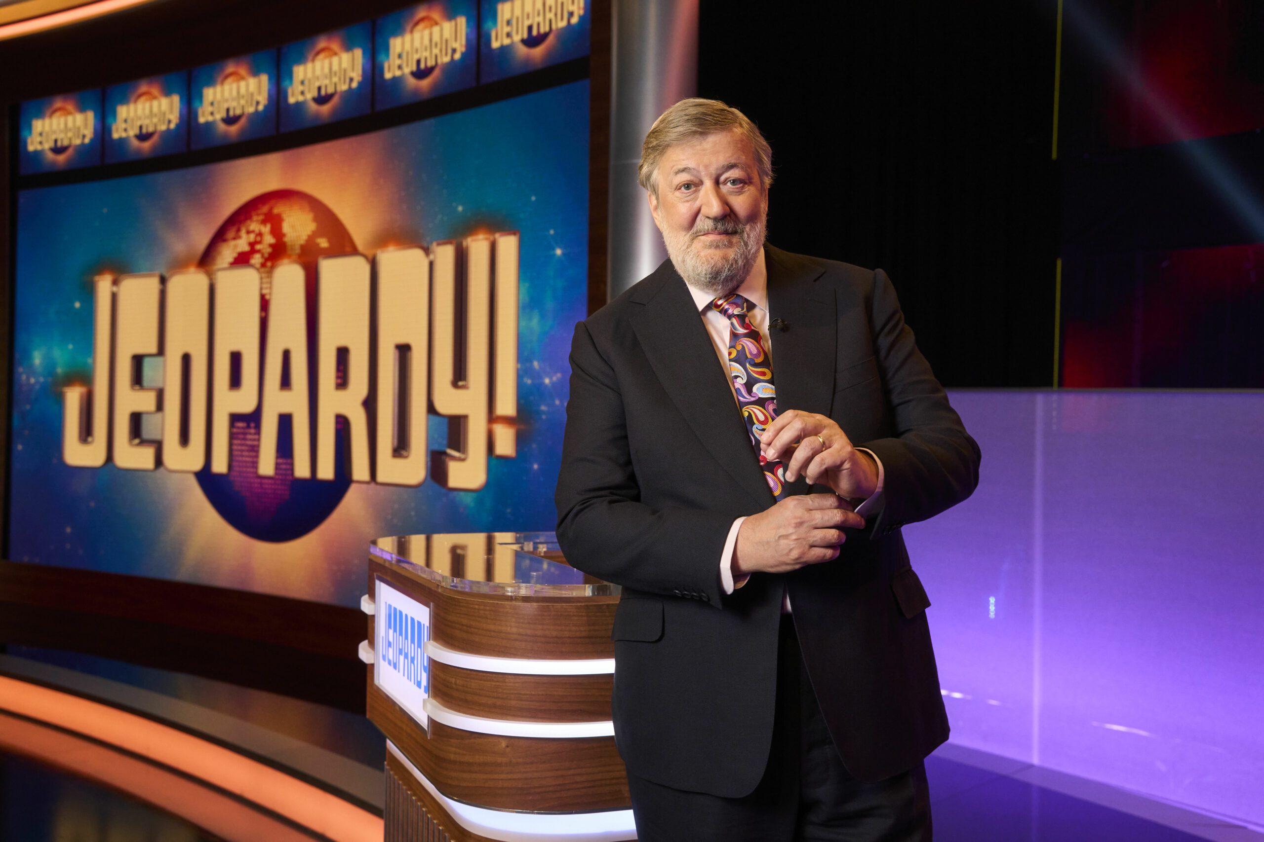 Stephen Fry in front of the Jeopardy logo