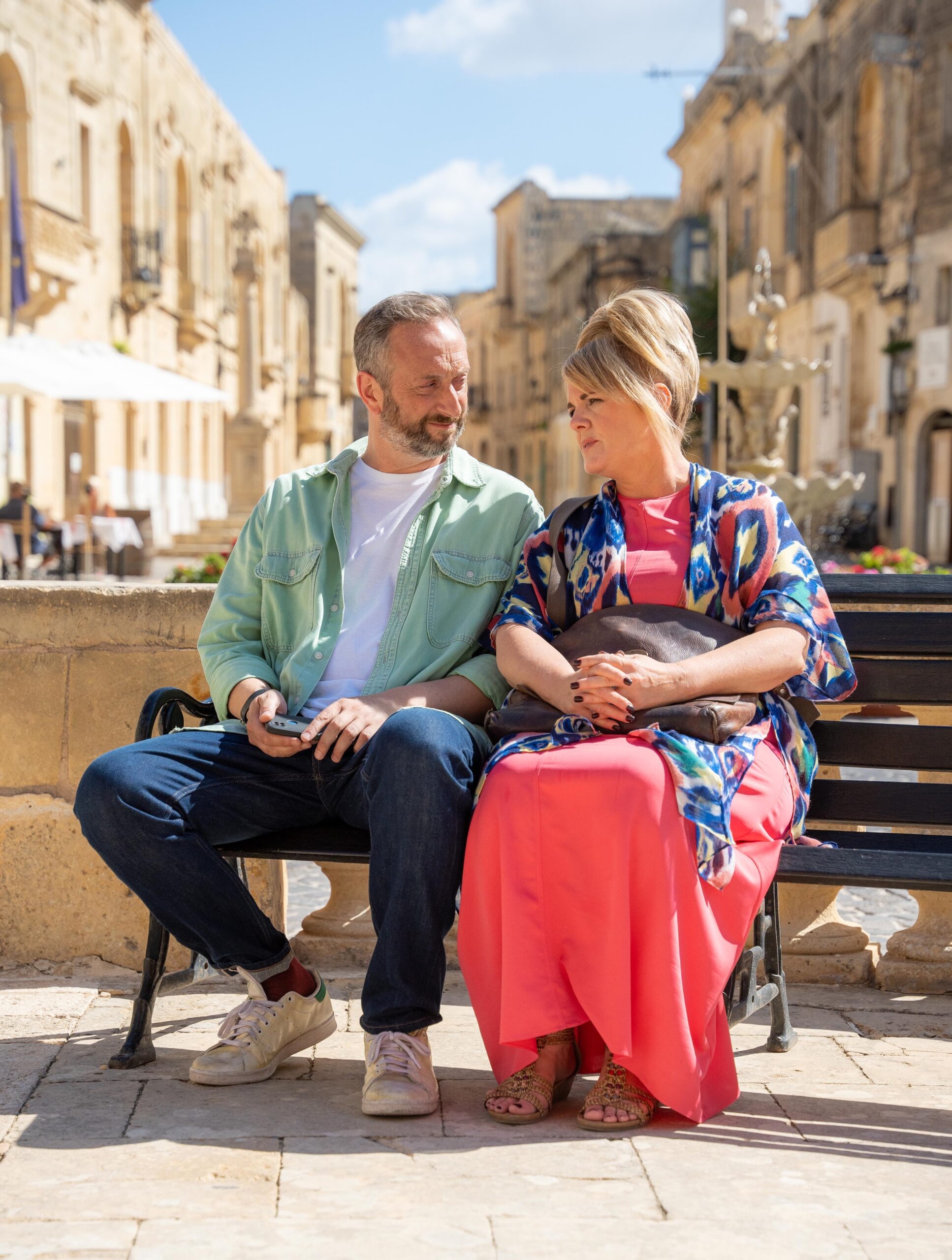 Steve Edge and Sally Lindsay sit on bench in character for Madame Blanc Mysteries