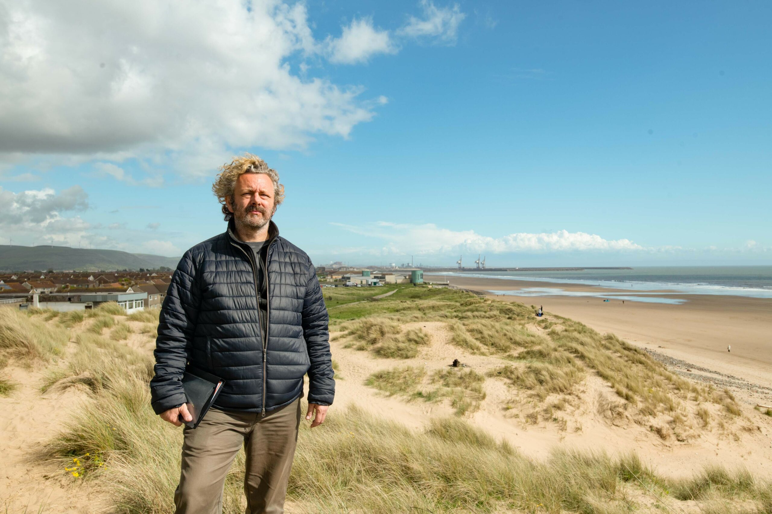 Behind-the-scenes image of director-actor Michael Sheen on The Way, wearing a coat and standing in the Welsh countryside
