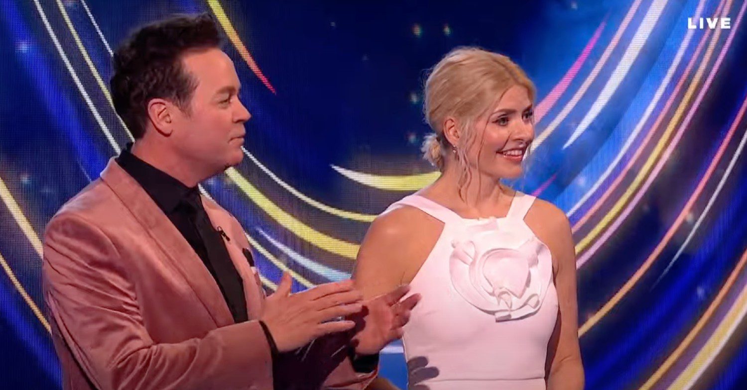 Holly Willoughby wearing a white dress with Stephen Mulhern in a bronze velvet suit presenting Dancing On Ice