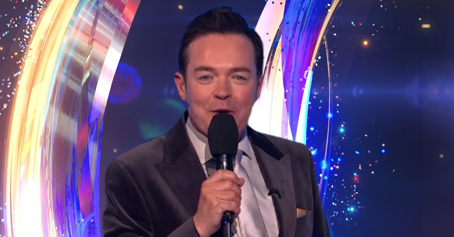 Stephen Mulhern speaking into microphone in front of Dancing On Ice logo