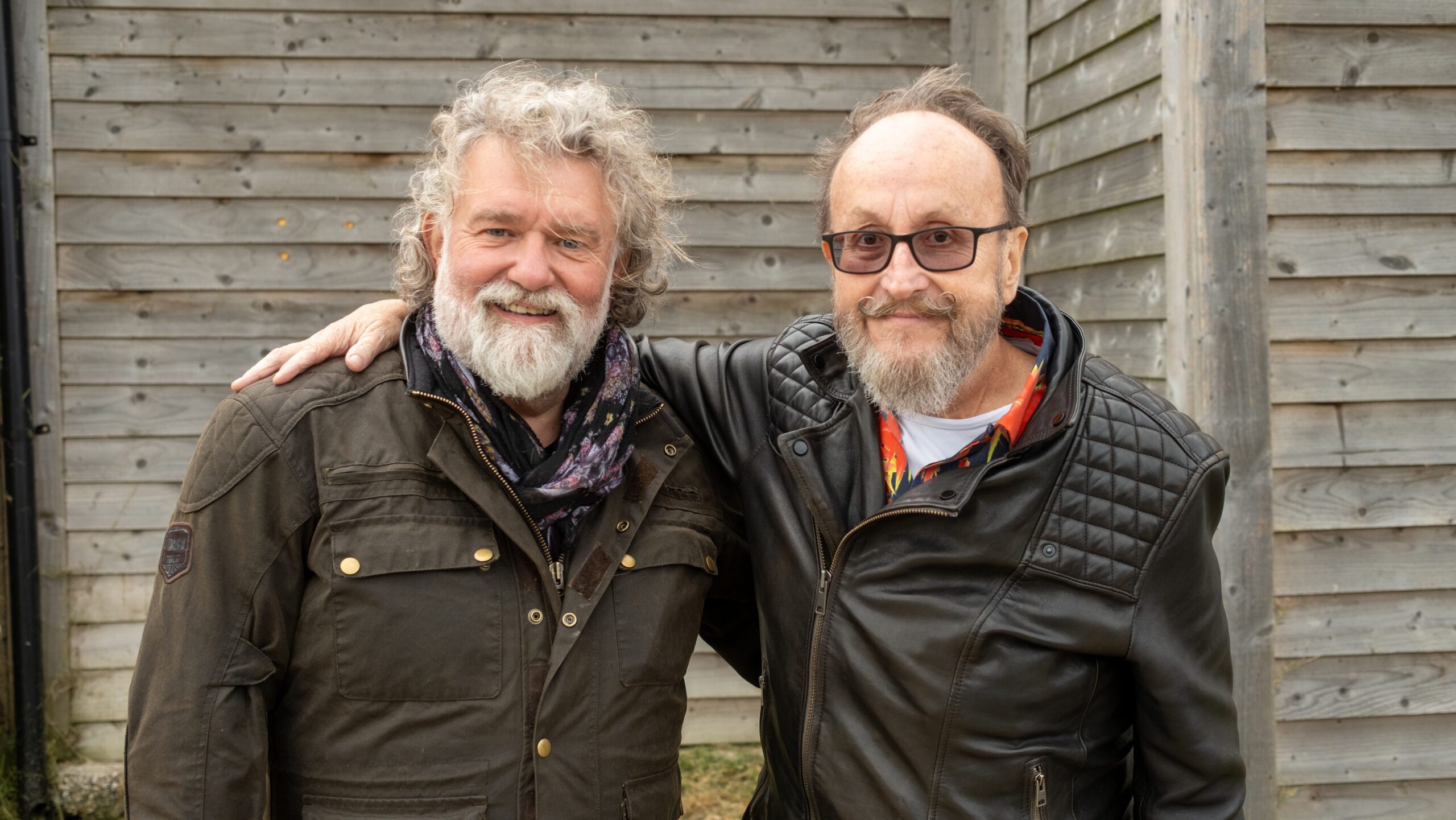 Si King and Dave Myers smiling against a fence
