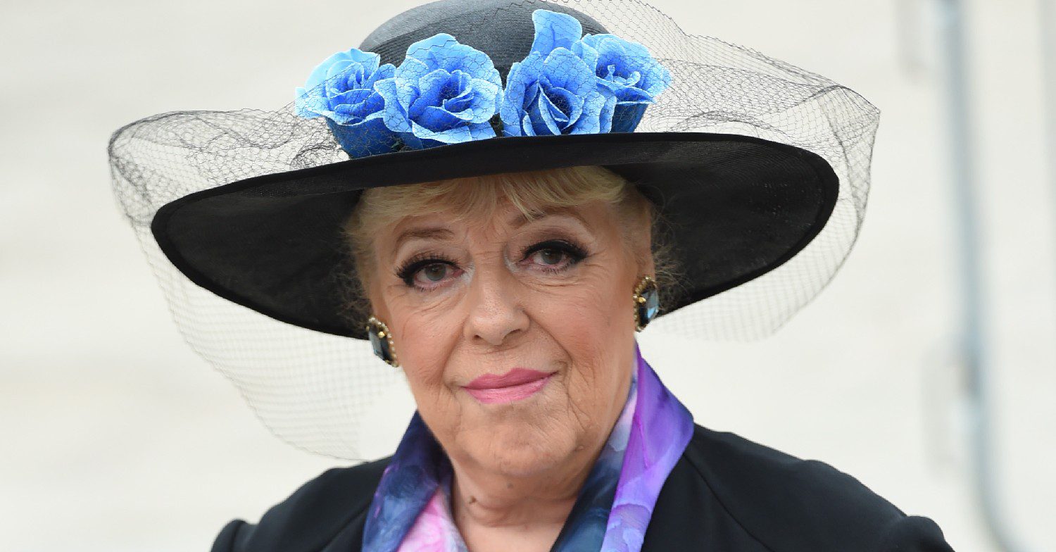 Julie Goodyear smiling with black hat on featuring blue flowers