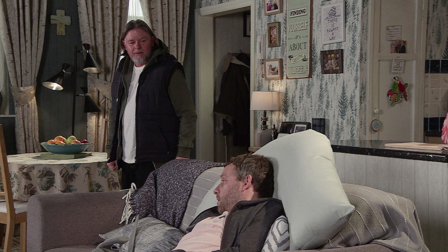 Denny looks at Paul slumped on the sofa in Corrie