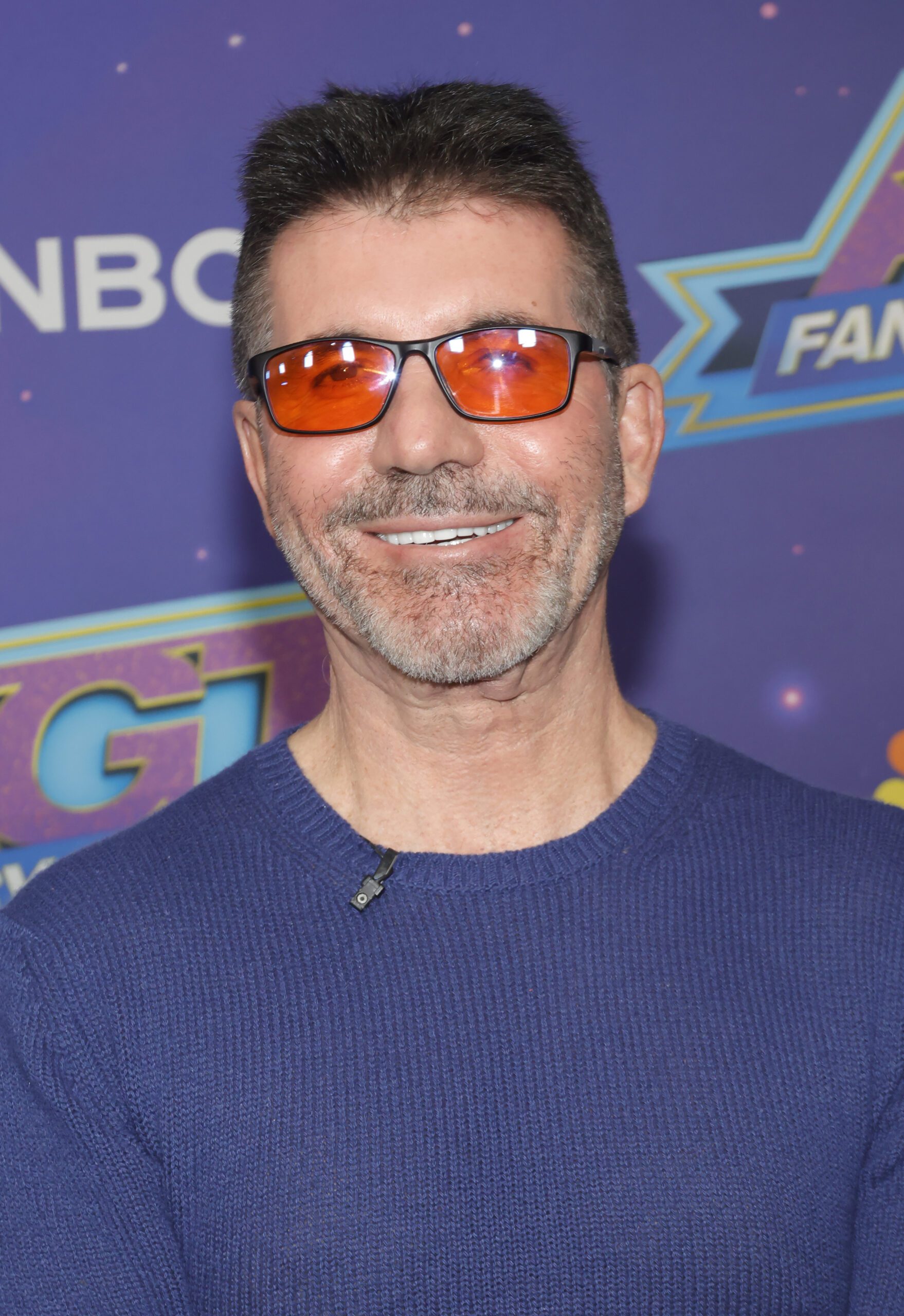 Simon Cowell smiling wearing red glasses