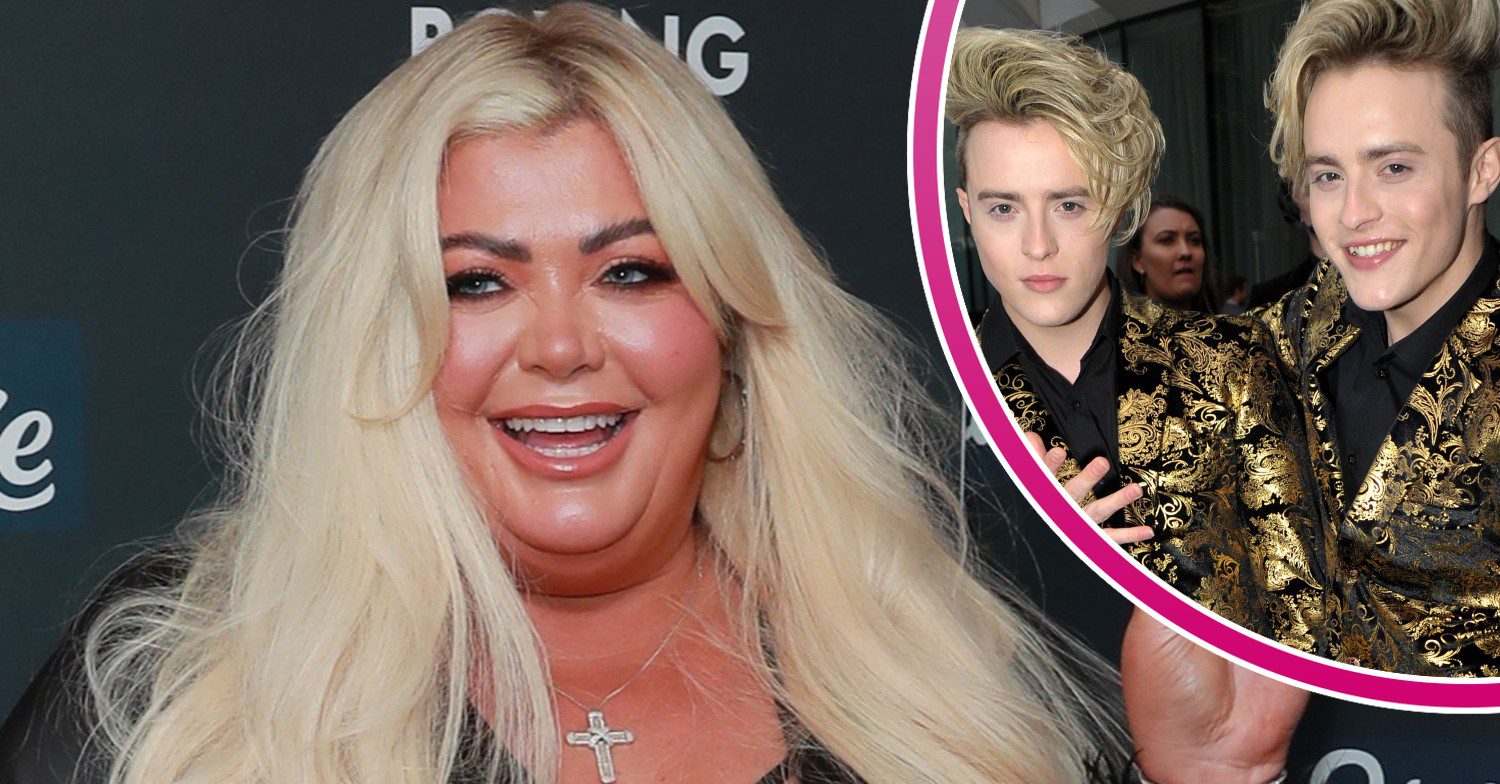 Gemma Collins in all black outfit showing peace sign and smiling with cut-out of Jedward posing in matching gold outfits