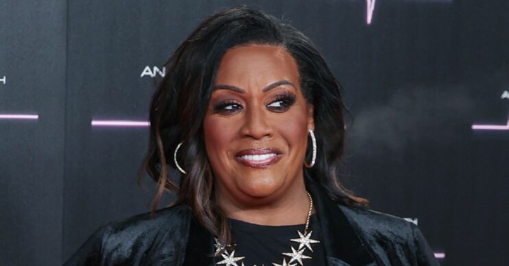 Alison Hammond smiling at a red carpet event, wearing black on a black background