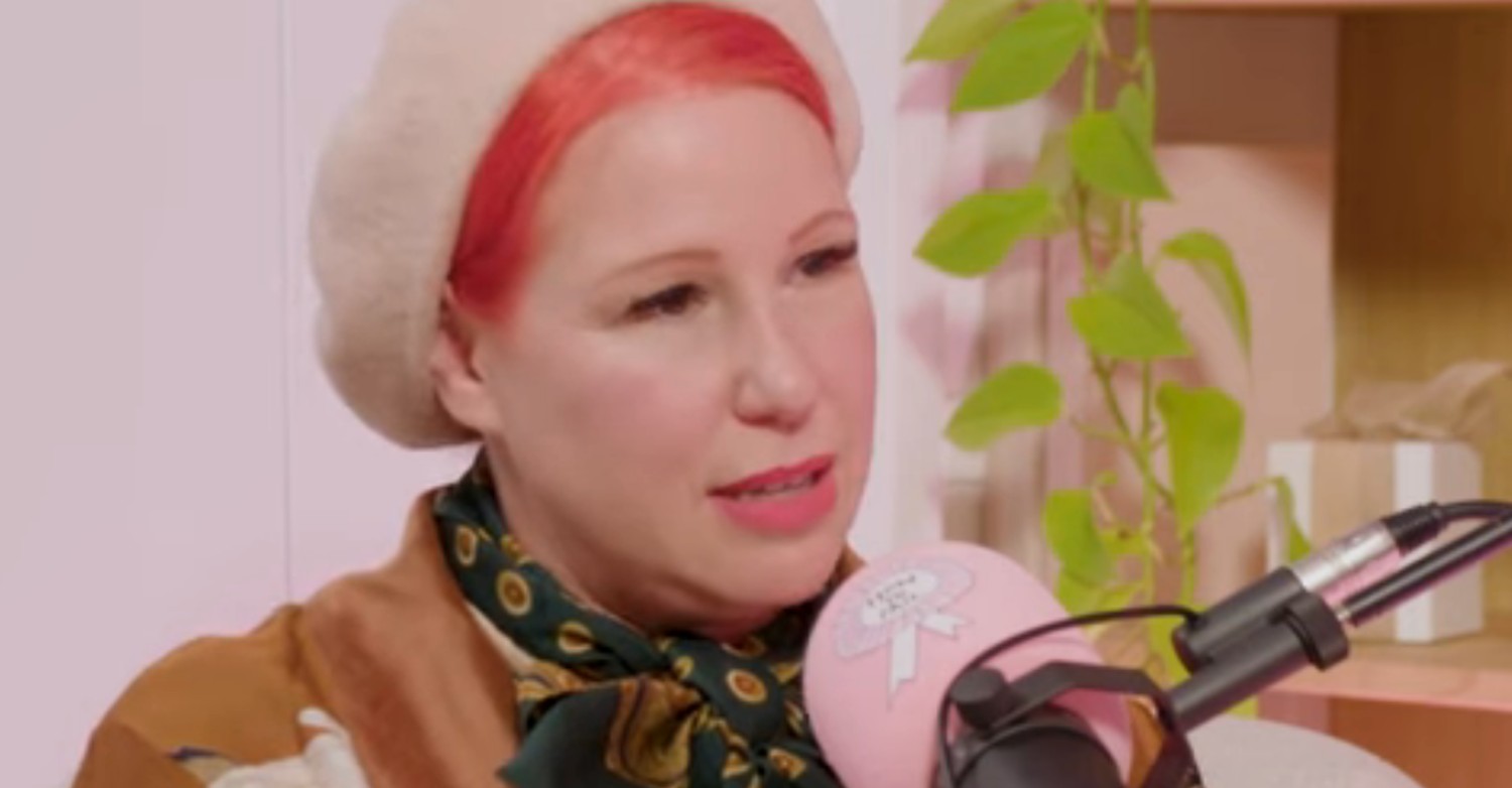 Angel Strawbridge frowning whilst wearing a beret on a pink podcast set, whilst chatting on Elizabeth Day's How to fail podcast