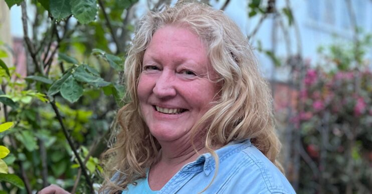 Charlie Dimmock smiling at the camera beside shrubbery