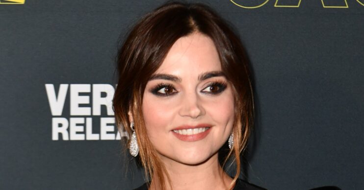 Jenna Coleman wearing black velvet dress on red carpet with up-do hairstyle whilst smiling