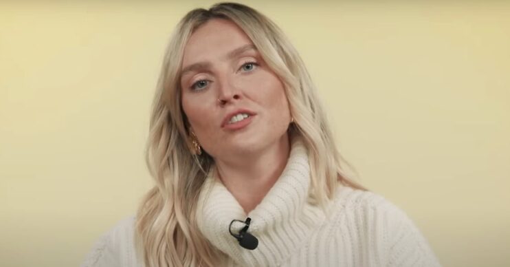 Perrie Edwards speaking. She is wearing a white turtleneck knitted jumper