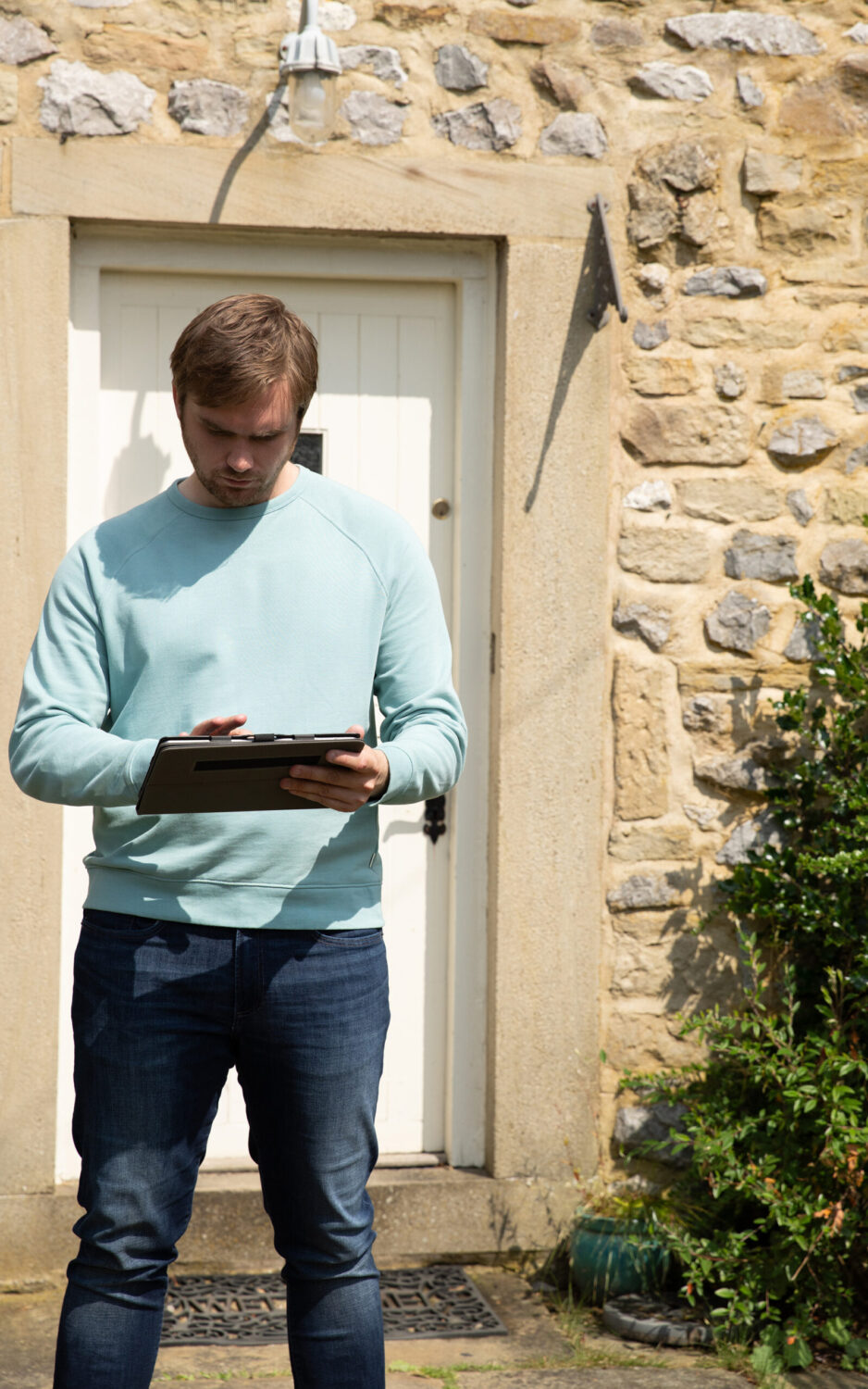 Emmerdale's Tom is standing outside of the door on his tablet