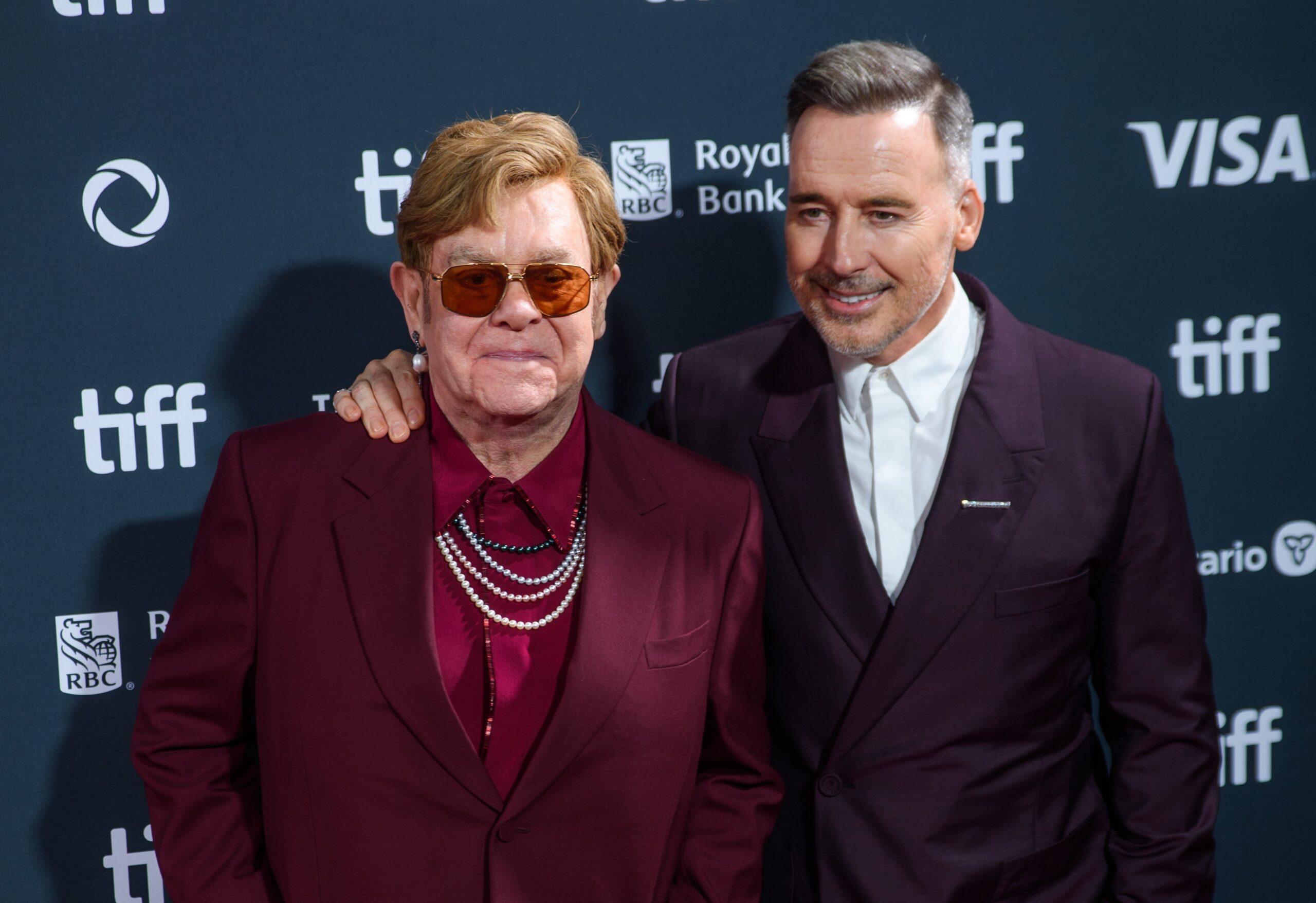Elton John smiling with husband David at event
