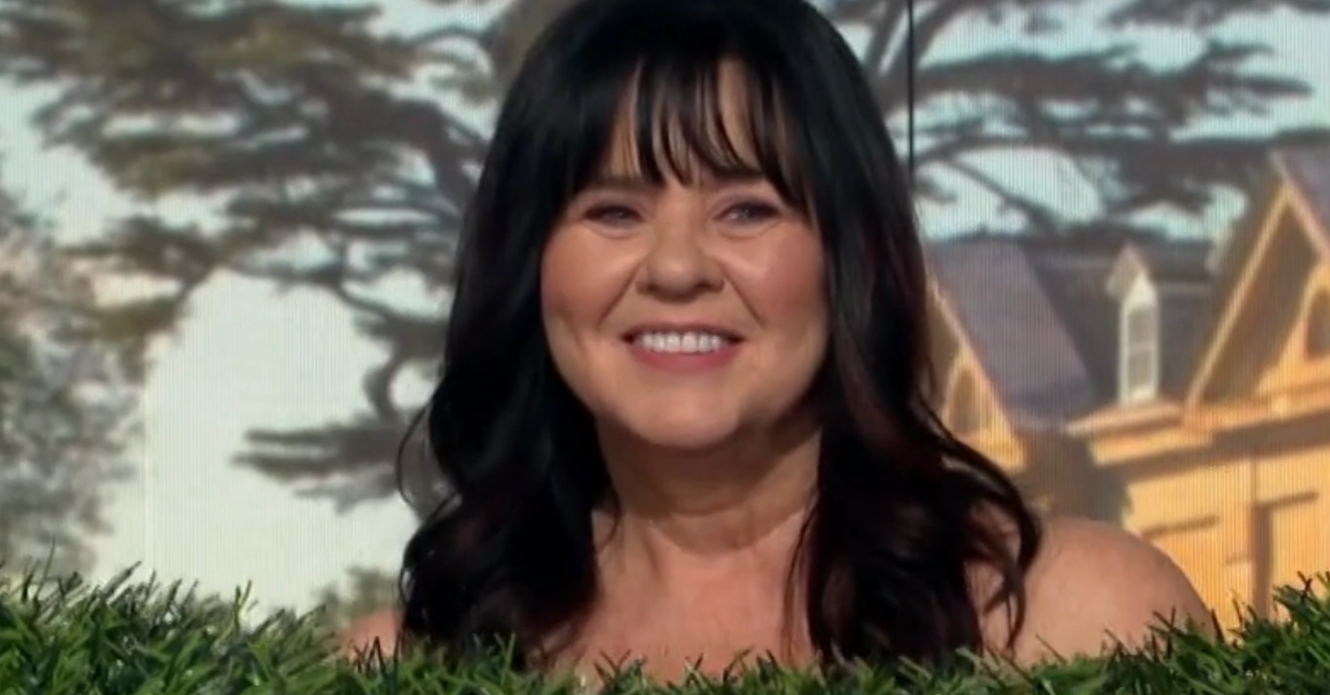 Coleen Nolan smiling with bare shoulders and green shrubbery covering her chest